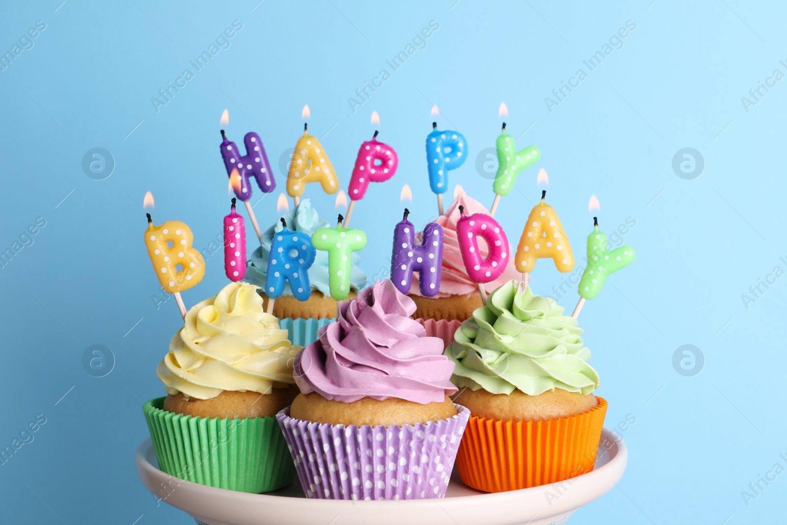 Photo of Birthday cupcakes with burning candles on stand against light blue background
