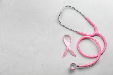 Photo of Pink ribbon and stethoscope on light grey stone background, flat lay with space for text. Breast cancer concept