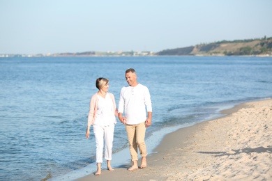 Happy mature couple walking at beach on sunny day