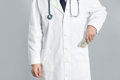 Photo of Doctor putting bribe into pocket on grey background, closeup. Corruption in medicine