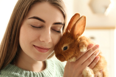 Photo of Young woman with adorable rabbit indoors, closeup. Lovely pet