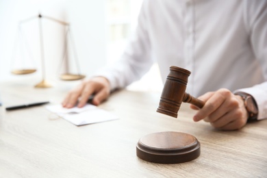 Photo of Judge with gavel at table in courtroom, closeup. Law and justice concept