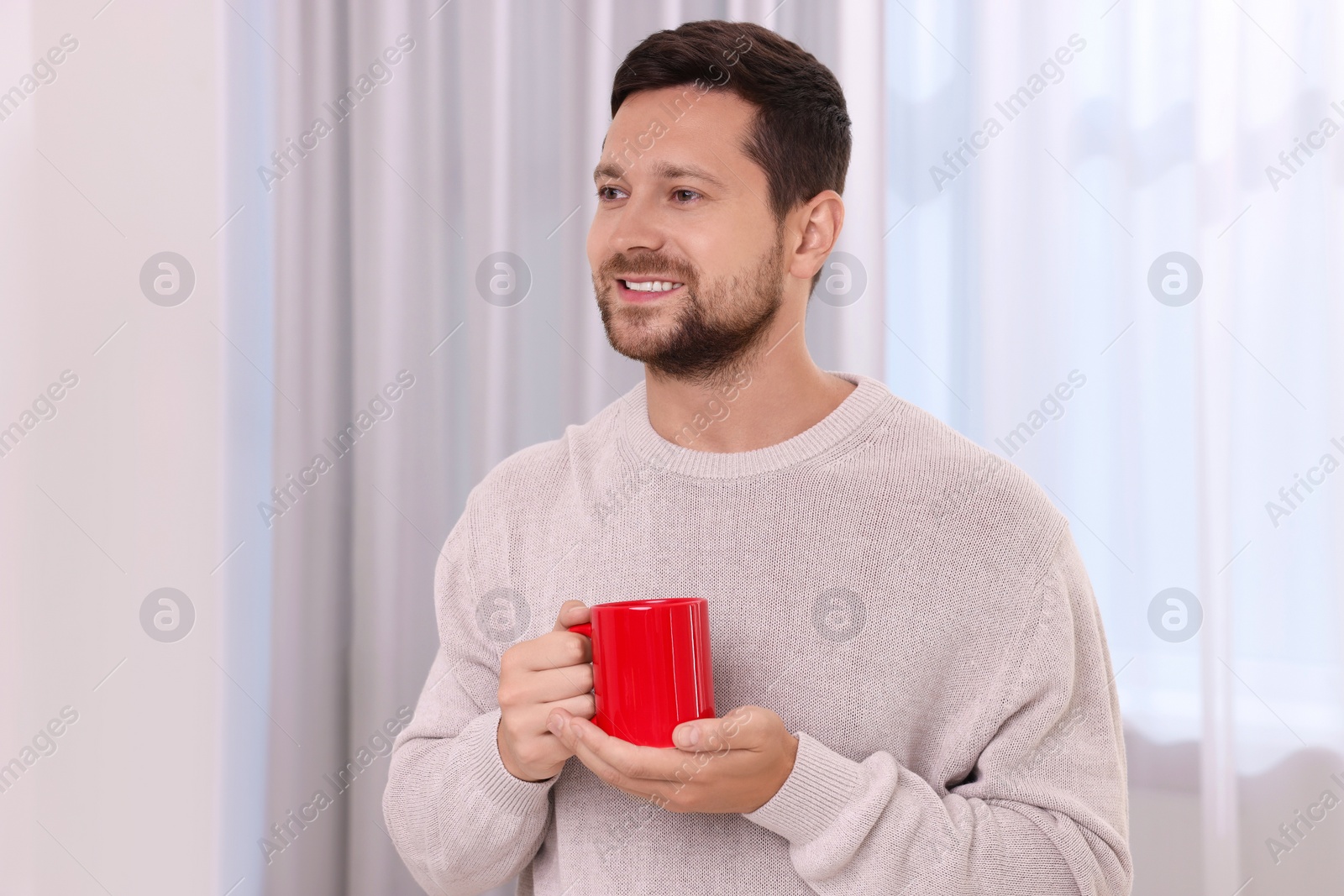 Photo of Happy man holding red ceramic mug at home