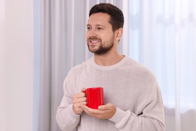 Photo of Happy man holding red ceramic mug at home