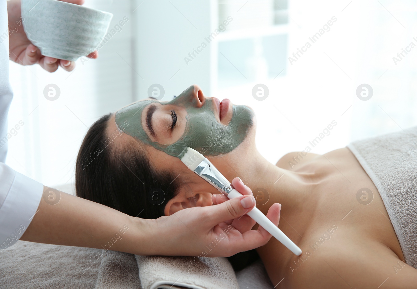 Photo of Cosmetologist applying mask on client's face in spa salon