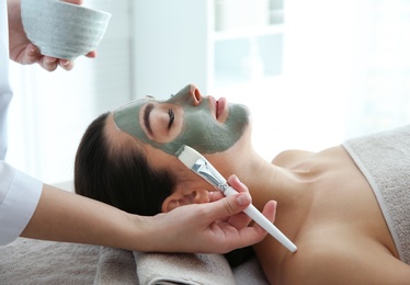 Photo of Cosmetologist applying mask on client's face in spa salon