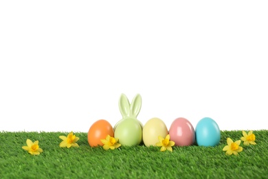 Photo of Dyed Easter eggs and bunny ears on green grass against white background