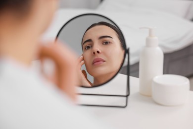 Woman with dry skin looking at mirror indoors