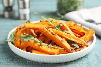 Photo of Plate with baked sweet potato slices and arugula on wooden table, closeup