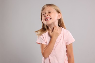 Photo of Suffering from allergy. Little girl scratching her neck on light gray background, space for text