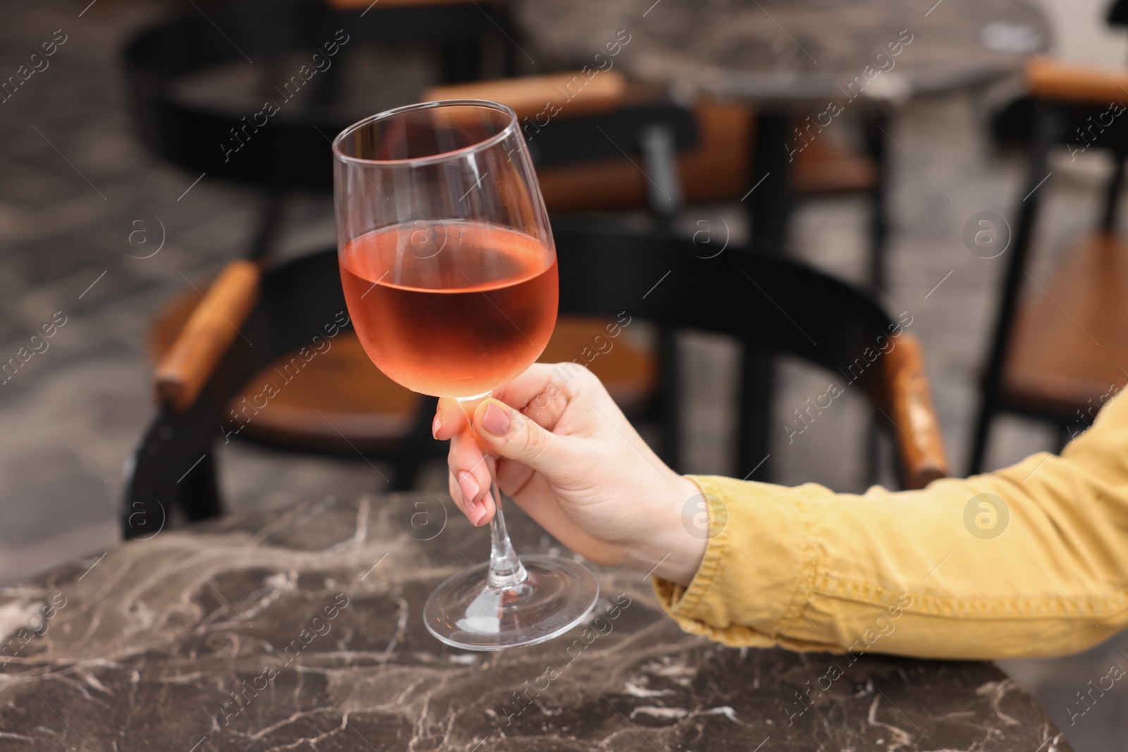 Photo of Woman holding glass of rose wine at dark marble table in outdoor cafe, closeup