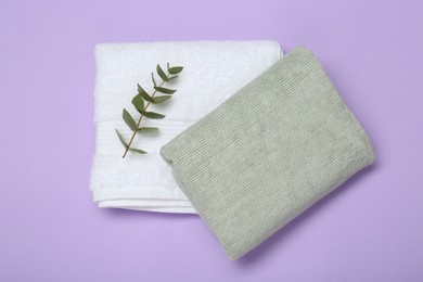 Different soft towels and eucalyptus branch on violet background, top view