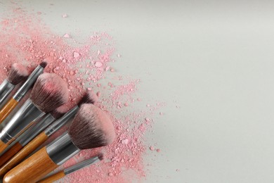 Photo of Makeup brushes and scattered eye shadows on light grey background, flat lay. Space for text