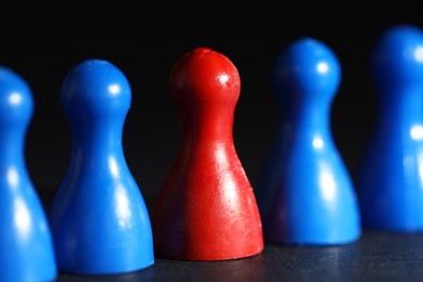 Photo of Choice concept. Red pawn among blue ones on black table, closeup