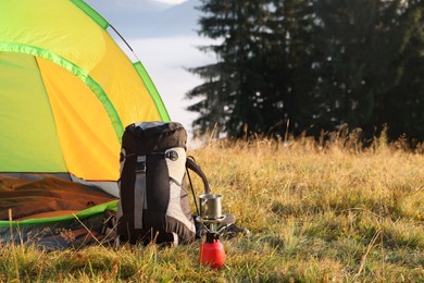 Photo of Camping tent, backpack and burner with metal mug outdoors. Space for text