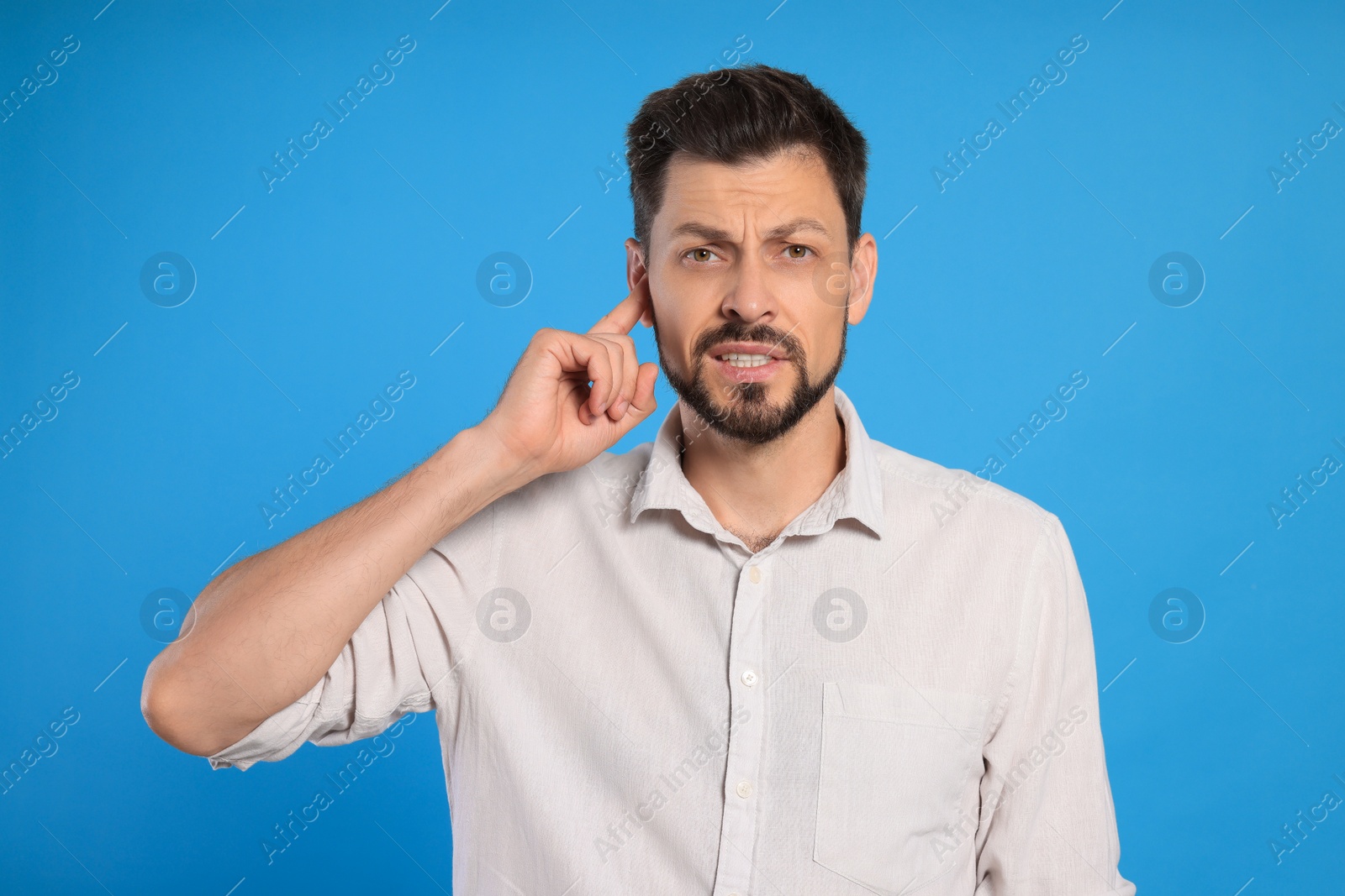 Photo of Man suffering from ear pain on light blue background