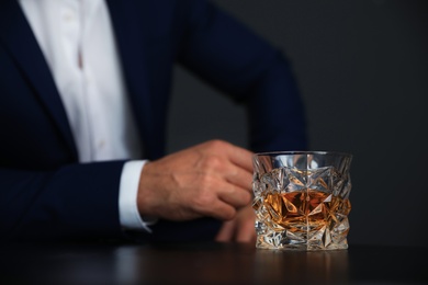 Young man with glass of whiskey at table, closeup view. Space for text