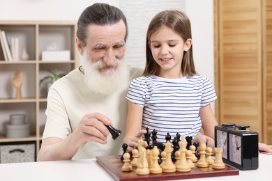 Photo of Senior man teaching his granddaughter to play chess at home