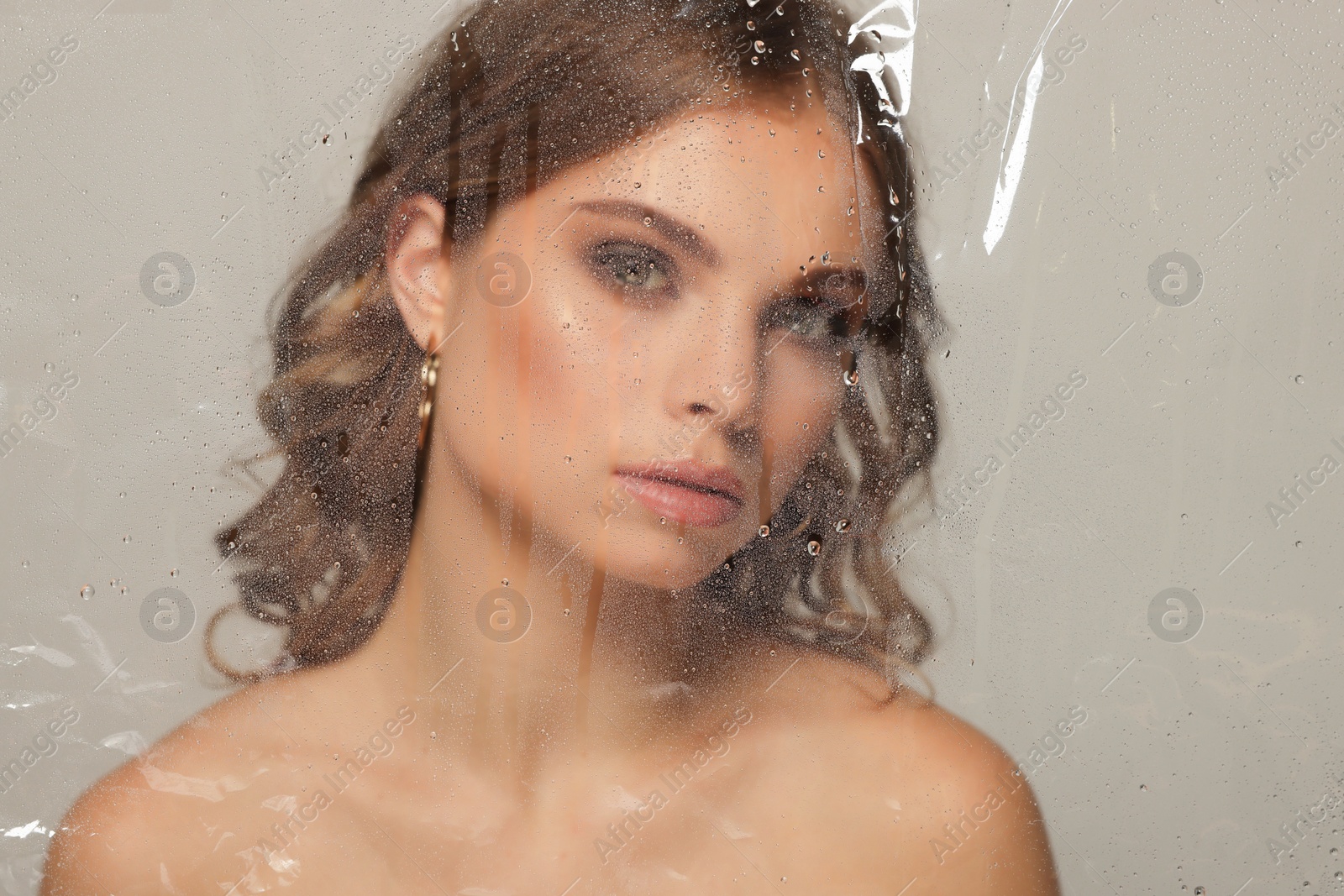 Photo of Beautiful young woman posing through transparent film on grey background