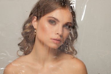 Beautiful young woman posing through transparent film on grey background