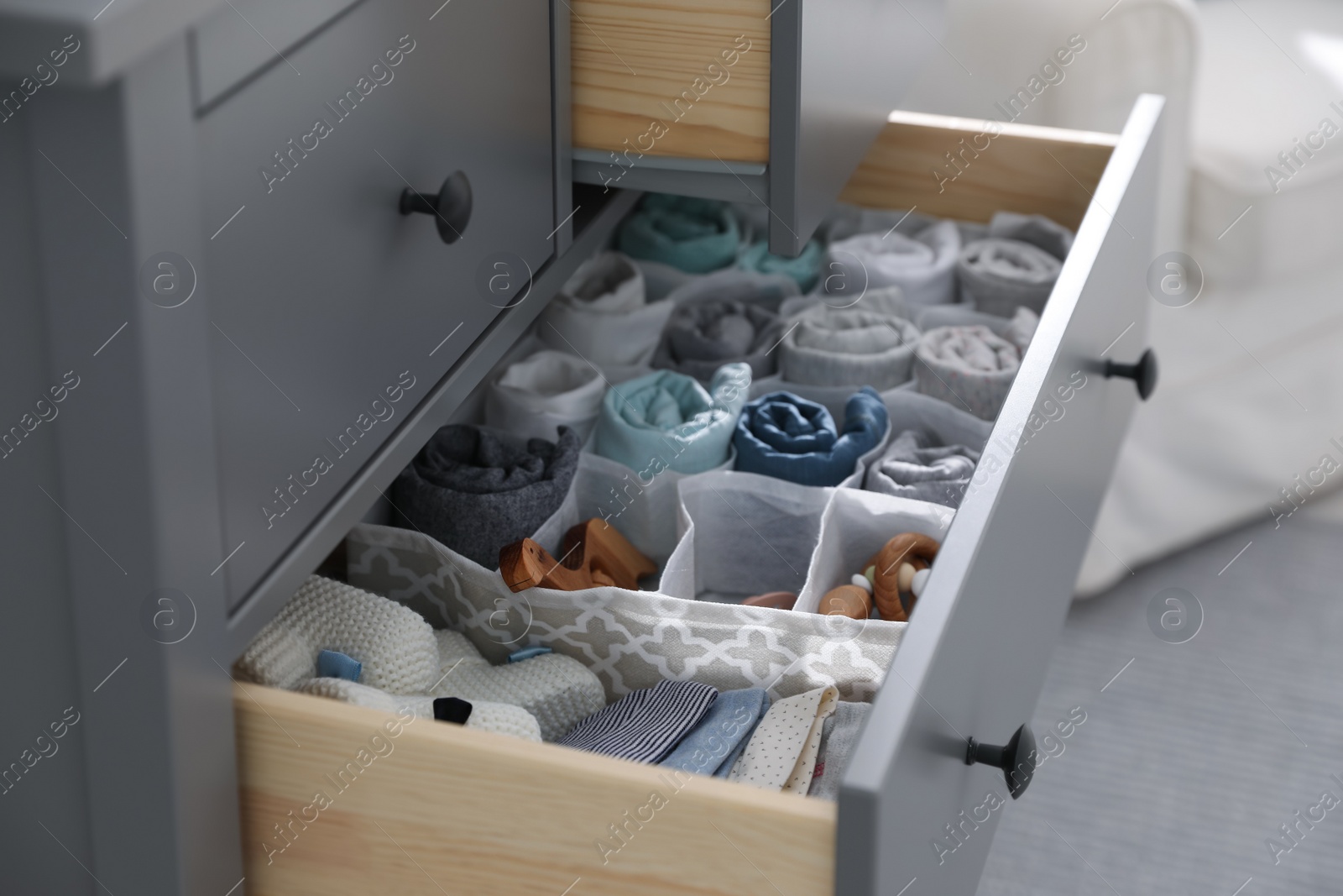 Photo of Modern open chest of drawers with baby clothes and accessories in room, closeup