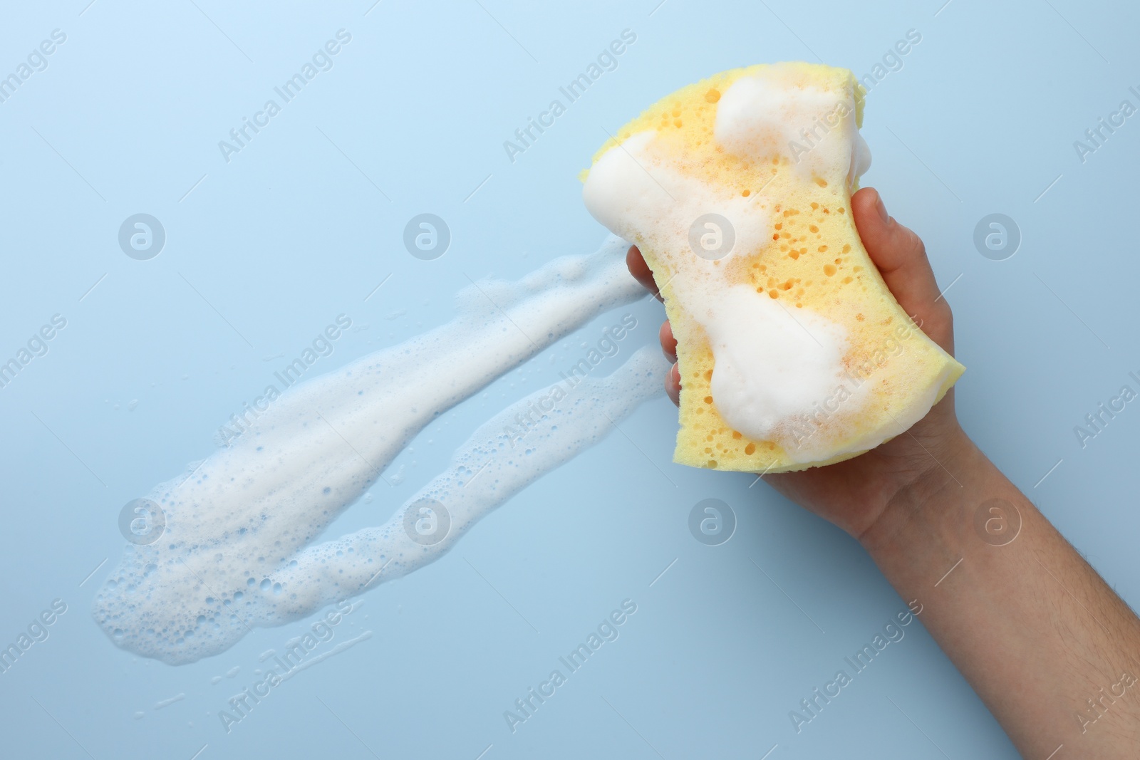 Photo of Man holding sponge with foam on light blue background, top view