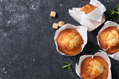 Delicious sweet muffins and brown sugar on black textured table, flat lay. Space for text