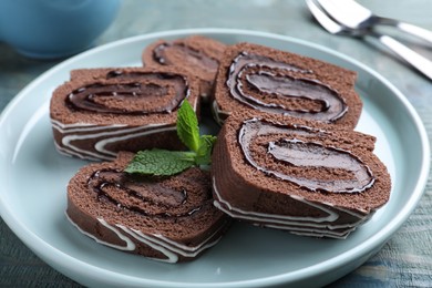 Photo of Tasty chocolate cake roll with cream and mint on blue wooden table, closeup