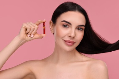 Beautiful young woman with long healthy hair holding ampoule on pink background