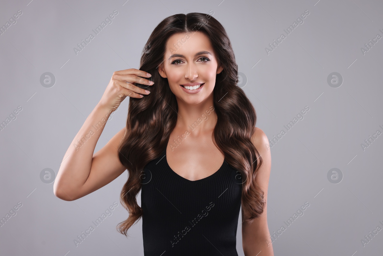 Image of Gorgeous woman with shiny wavy hair on grey background. Professional hairstyling