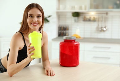 Photo of Young woman drinking protein shake at table indoors