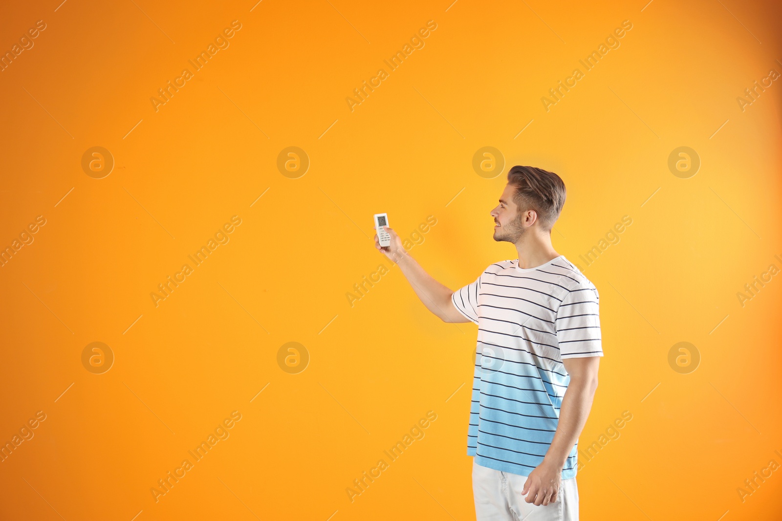 Photo of Young man with air conditioner remote on color background