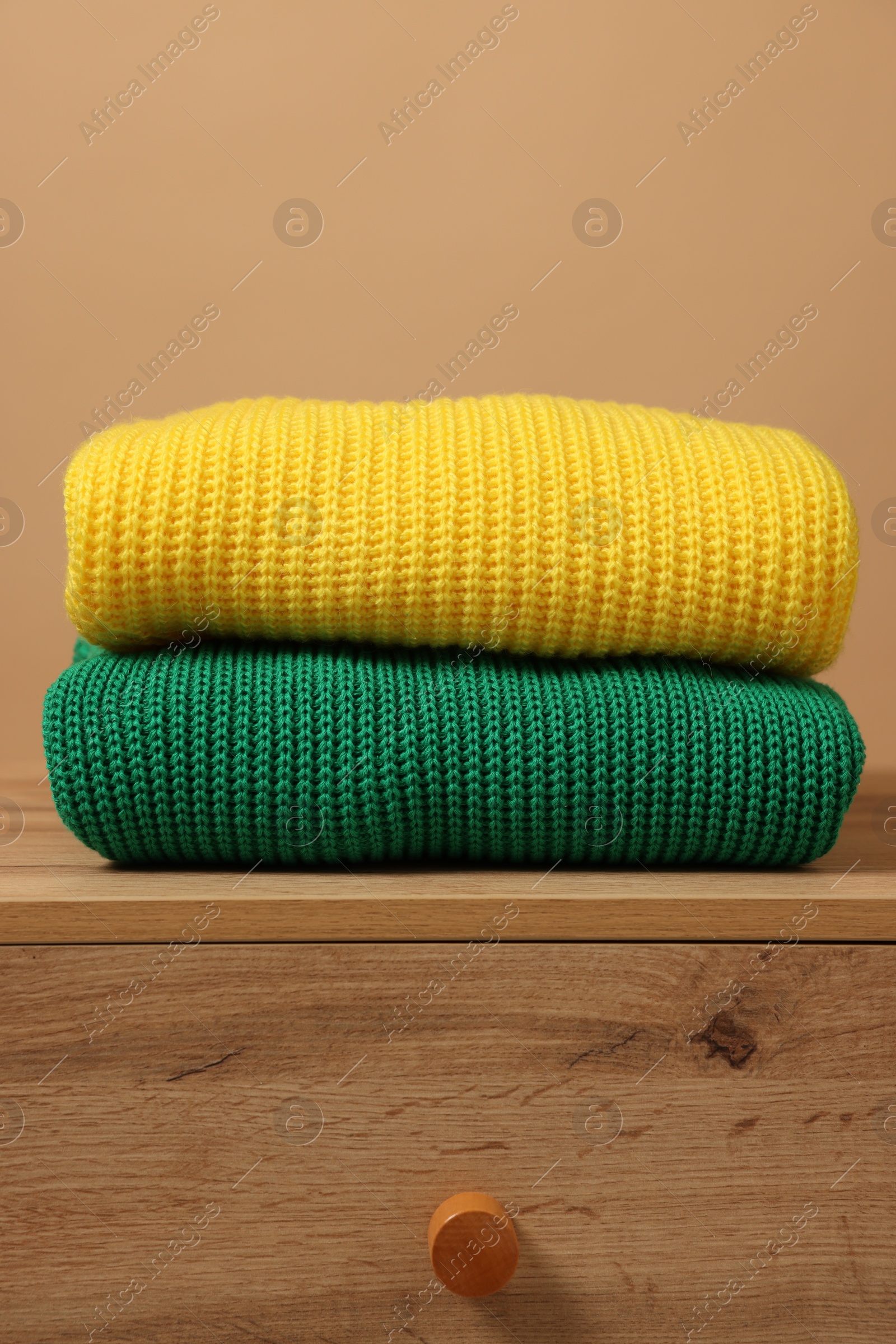 Photo of Different casual sweaters on chest of drawers against light brown background