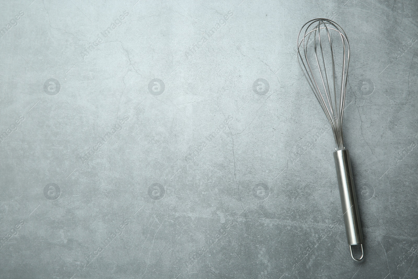 Photo of Metal whisk on gray table, top view. Space for text