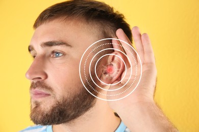 Young man with hearing problem on yellow background