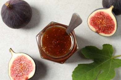 Photo of Glass jar with tasty sweet jam, green leaf and fresh figs on white table, flat lay