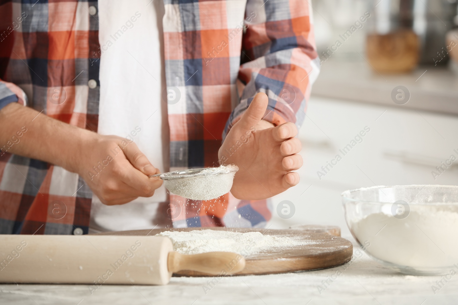 Photo of Man sprinkling flour over board on table in kitchen