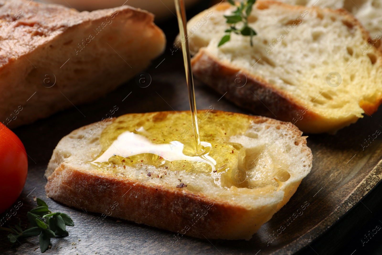 Photo of Pouring oil onto slices of bread on wooden plate, closeup