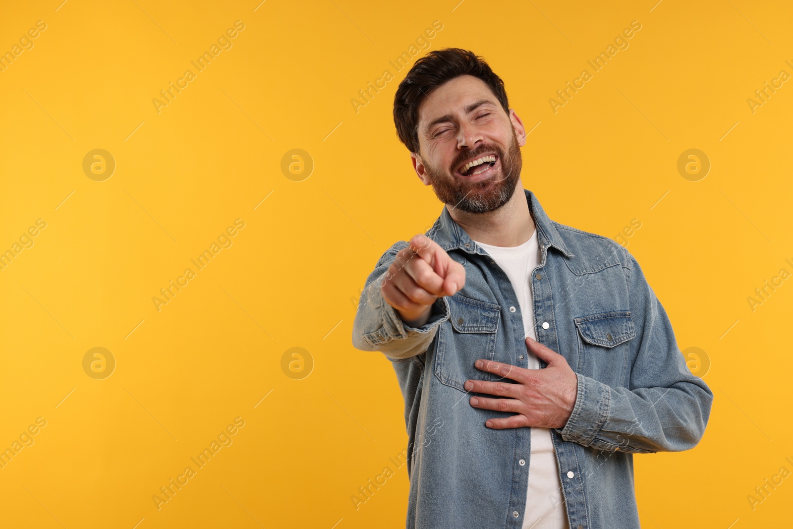 Photo of Handsome man pointing at something and laughing on yellow background. Space for text