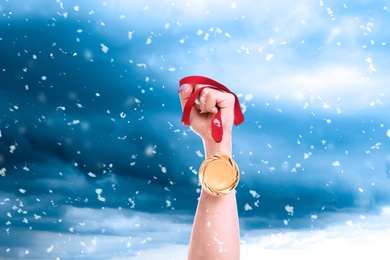 Image of Winner raising hand with gold medal up to sky on snowy day, closeup