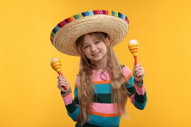 Cute girl in Mexican sombrero hat with maracas on orange background