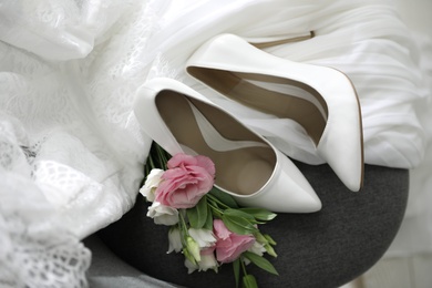 Photo of Pair of white high heel shoes, flowers and wedding dress on chair, above view