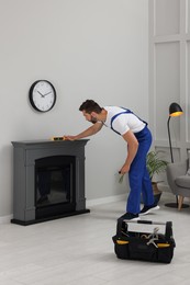 Photo of Professional technician using construction level for installing electric fireplace in room