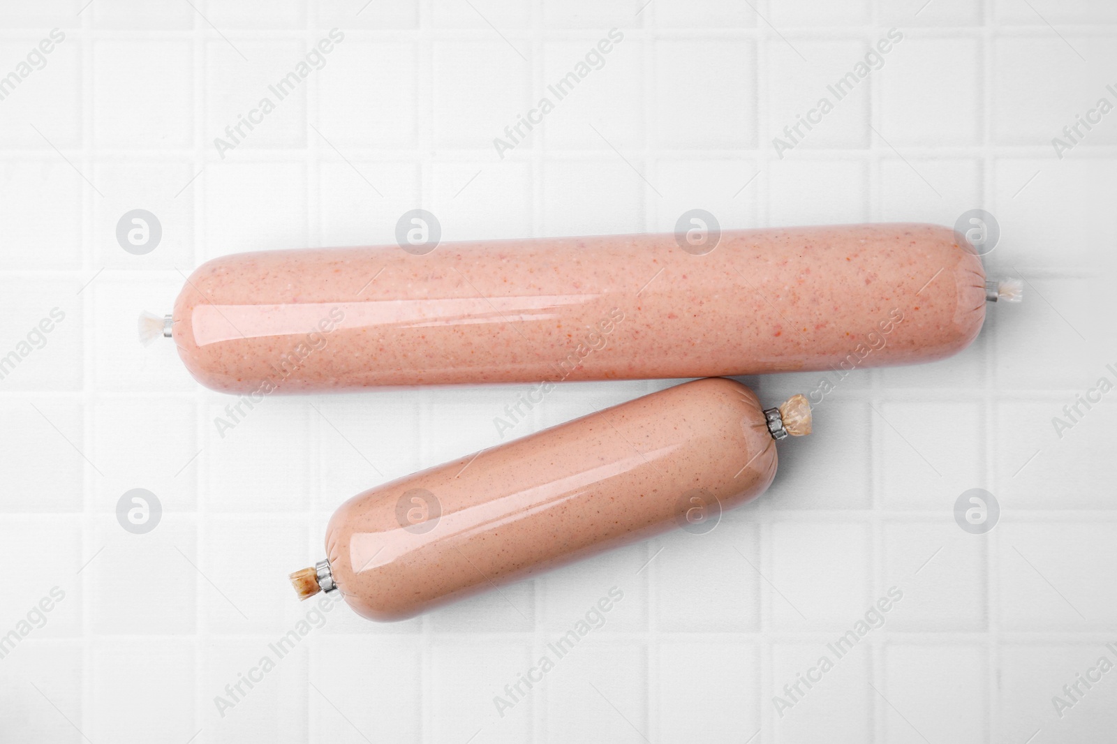 Photo of Delicious liver sausages on white tiled table, flat lay