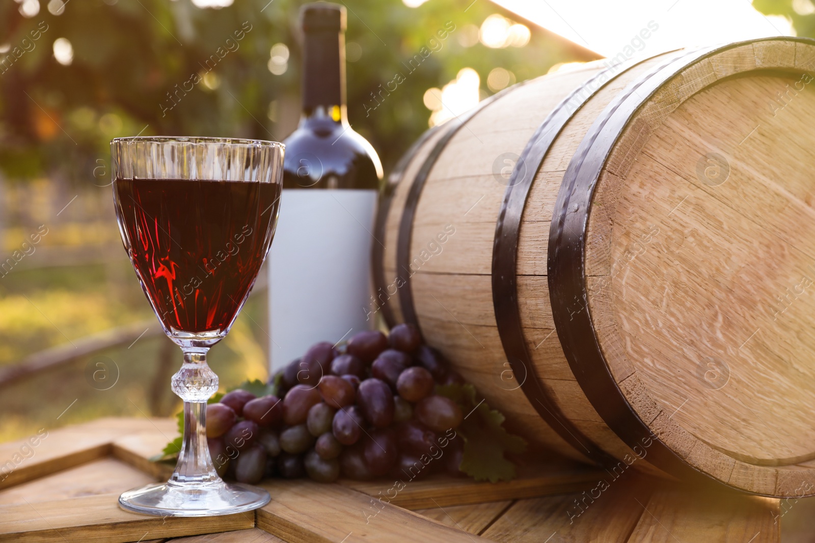 Photo of Composition with wine and ripe grapes on wooden table in vineyard