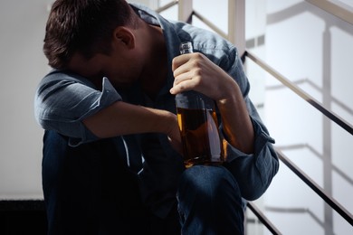 Addicted drunk man with alcoholic drink on stairs indoors