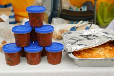 Photo of Volunteer food distribution. Containers with tasty adjika sauce near pie served on table outdoors