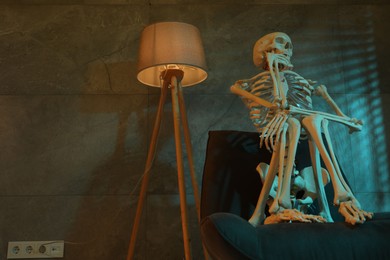 Photo of Waiting concept. Human skeleton sitting in armchair indoors, space for text