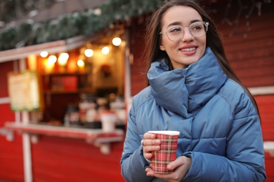 Photo of Woman with cup of mulled wine at winter fair. Space for text
