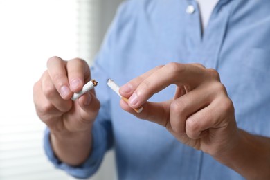 Photo of Stop smoking concept. Man holding pieces of broken cigarette indoors, closeup